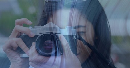 Holding silver film camera at right eye, Asian woman framing shot in garden, with light streaks
