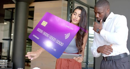 Pointing colleagues examining virtual purple bank card graphic in office lobby, with tablet