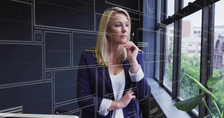 Standing businesswoman in blazer gazing by large office window, with translucent tech grid overlay