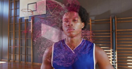 Standing player in blue jersey displaying red particle sphere in school gym, with hoop and bars