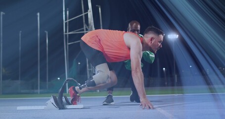 Anchoring runner wearing orange top using running blade in blocks on blue track under floodlights
