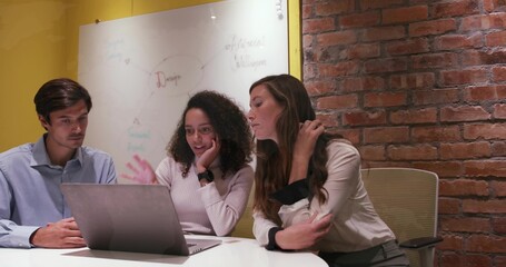 Collaborating colleagues reviewing laptop at table in meeting room, with whiteboard mind-map