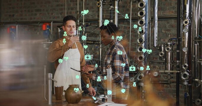 Holding tasting glass apron-clad worker inspecting liquor at distillery bench with tablet