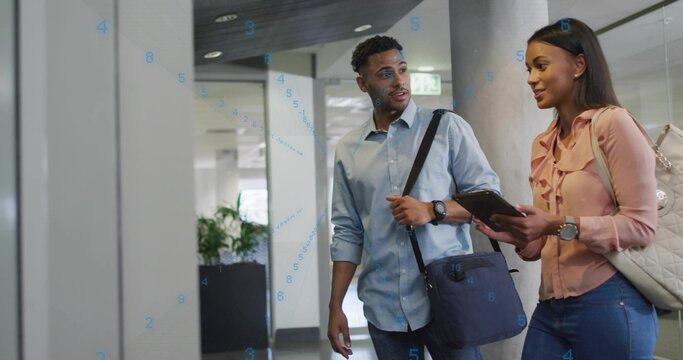 Walking business professionals discussing data on tablet in office corridor, with floating graphics