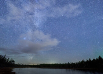 Milky way and clouds over the forest lake