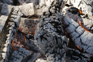 Bonfire concept with char on wood with glowing flame over firewood closeup.