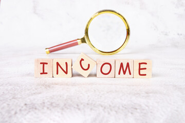 Blocks spelling out income sit on a soft surface, while a magnifying glass emphasizes the word, inviting viewers to explore financial concepts and opportunities in depth