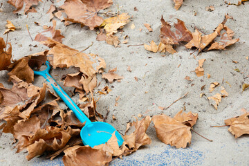 Blue shovel in sandbox with autumn leaves