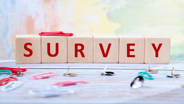 Brightly colored paper clips and pushpins are placed around wooden blocks that spell out the word survey, adding a playful touch to a creative workspace filled with vibrant backgrounds