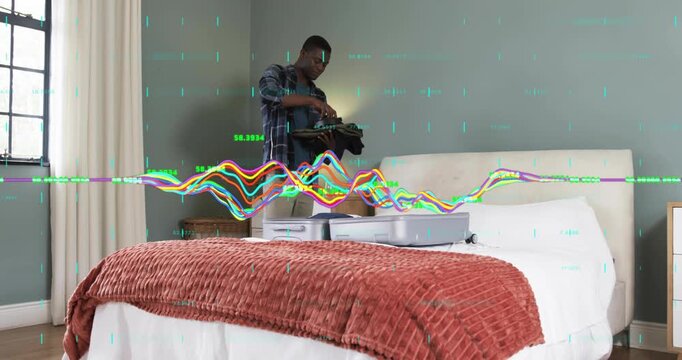 Man entering bedroom carrying folded clothes, placing garments flat inside open suitcase for travel