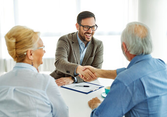 Obraz premium Portrait of a businessman or real estate agent or doctor shaking hands and signing a deal contract with senior couple in his office