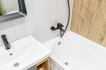 A modern bathroom featuring a white sink and bathtub with black fixtures, complemented by light gray and wood-patterned tiles. The space is clean, bright, and well-maintained
