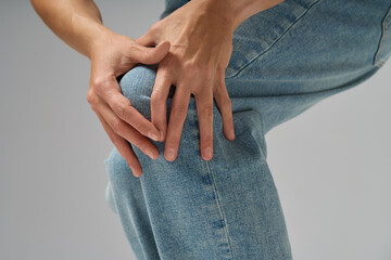 Close-up of woman holding her knee feeling joint pain wearing jeans indoors