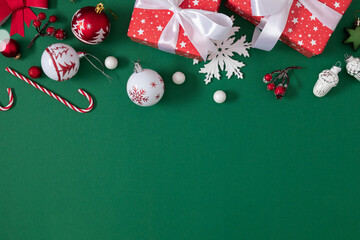 Flat lay Christmas composition with red gifts, white ornaments, and candy canes on green background. Elegant festive layout for greeting cards, holiday banners, and winter design.