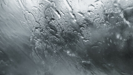 Fototapeta premium Raindrops on glass, creating a mesmerizing abstract pattern. The water droplets reflect light and distort the view, capturing a sense of both calm and movement.