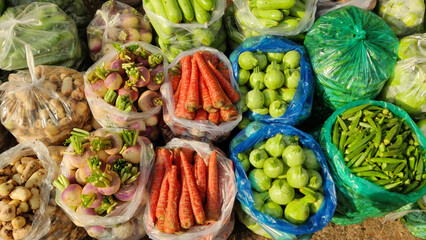 A vibrant assortment of fresh vegetables displayed in plastic bags at a market including carrots...