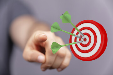 Close-up of a hand pointing at a target, darts hitting the bullseye representing success, goal...