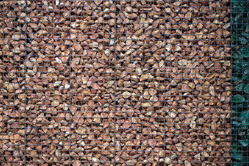 Gabion wall filled with brown stones and metal mesh texture