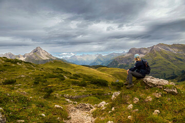 Ein Wanderer sitzt auf einem H&uuml;gel mit Blick auf eine bergige Landschaft unter grau bew&ouml;lktem Himmel, Schr&ouml;cken, &Ouml;sterreich, Europa