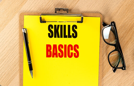 SKILLS BASICS text on bright yellow clipboard with pen and eyeglasses on wooden desk