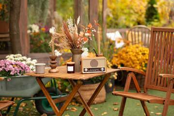 Outdoor autumn cozy setting with vintage radio, flowers, and coffee on a wooden table.