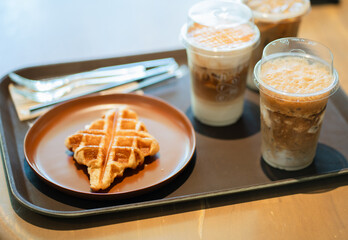 Close up and selective focus glasses of iced coffee with croffle in plate on tray in coffee shop.
