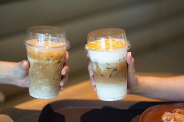 Hands of teenage girls holding glass of ice coffee together at cafe.