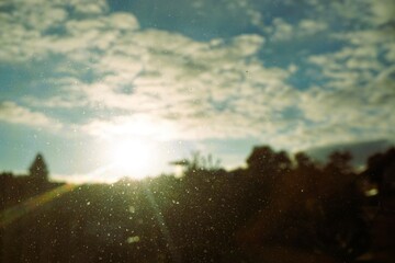 Abstraktes Landschaftspanorama mit untergehender Sonne über Silhouette von Reihe mit grünen bäumen und blauem Himmel mit weißem Wolkengebilde bei Sonnenuntergang auf dem Land am Abend im Sommer