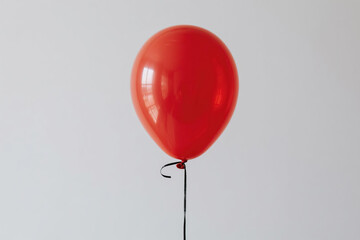 A single vibrant red balloon with a glossy surface and highlight reflection, tethered by a thin black string against a plain white background, symbolizing simplicity and joy.