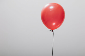 A single vibrant red balloon with a glossy surface and highlight reflection, tethered by a thin black string against a plain white background, symbolizing simplicity and joy.