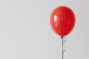 A single vibrant red balloon with a glossy surface and highlight reflection, tethered by a thin black string against a plain white background, symbolizing simplicity and joy.