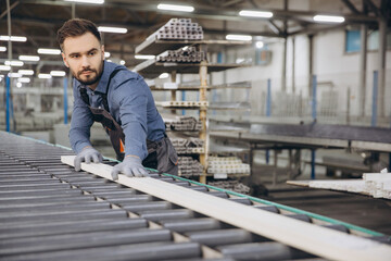 Factory worker placing wooden plank on assembly line in windows and doors production
