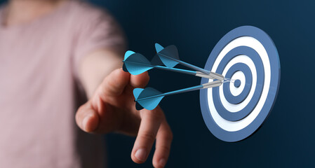 Image of hand pointing to a dartboard with three darts in the bullseye. Concept of hitting your...