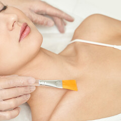 Asian female receiving skincare treatment with brush at spa.
