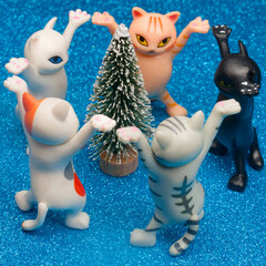 Cute toy kittens form a ring dance around a snowy Christmas tree on a blue glitter background;...