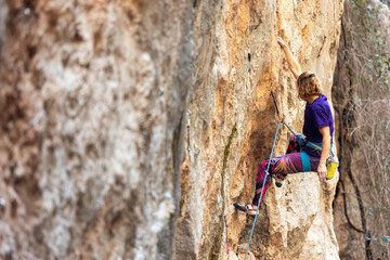 A woman climbs a rock, a strong girl trains strength and endurance, extreme sport, rock climbing on natural terrain, a rock climber climbs.