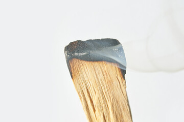 Close-up of burning palo santo stick with smoke against light background.