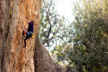woman climbing steep wall of rocky mountain. Girl climber overcomes challenging route.