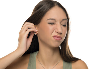 Studio shot of young woman with long brown hair wearing green tank top, scratching her ear with...