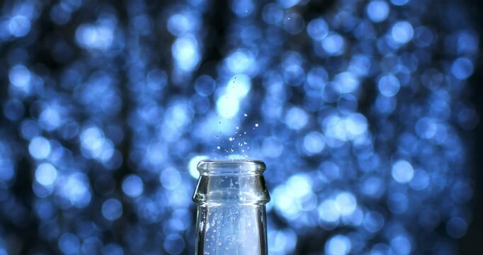 Slow Motion Close Uo of  Cork of champagne bottle is popping, surrounded by sparkling blue bokeh lights, symbol of anticipation, excitement and celebration at 1000 fps