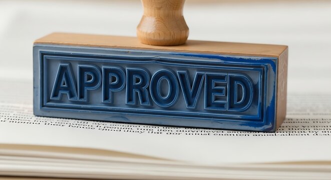 Close up of a blue rubber stamp with the word APPROVED in raised letters on a wooden handle, resting on a document.