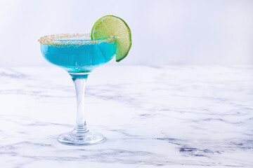 Bright blue cocktail with a slice of lime on a marble surface,