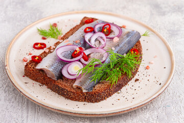 sandwiches , Herring fish, on dark rye bread, sprinkled with onion, chili pepper and herbs, on a light plate