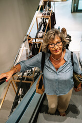 Senior woman shopping ascending escalator in clothing store