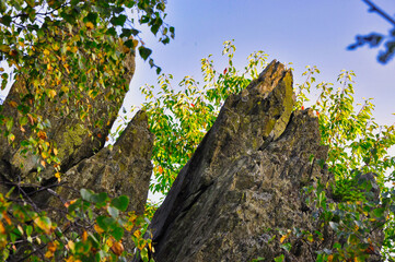 Okole - Góry Kaczawskie. Grupa skał na szczycie góry. Postrzępiona formacja skalna otoczona jesiennymi liśćmi pod jasnoniebieskim niebem. © Pol Badger