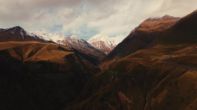 Aerial view of Stepantsminda town and majestic Mount Kazbek in Georgia under dramatic clouds and warm evening light.