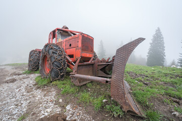 Old red tractor with chains in foggy mountain landscape.