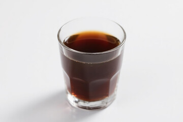 A transparent glass filled with rich, dark brown liquid, showcasing a smooth, glossy surface and a clear, visible base, elegantly positioned on a pure white background
