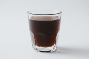 A transparent glass filled with rich, dark brown liquid, showcasing a smooth, glossy surface and a clear, visible base, elegantly positioned on a pure white background