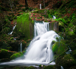 Obraz premium Mossy rocks and a waterfall in a forest.